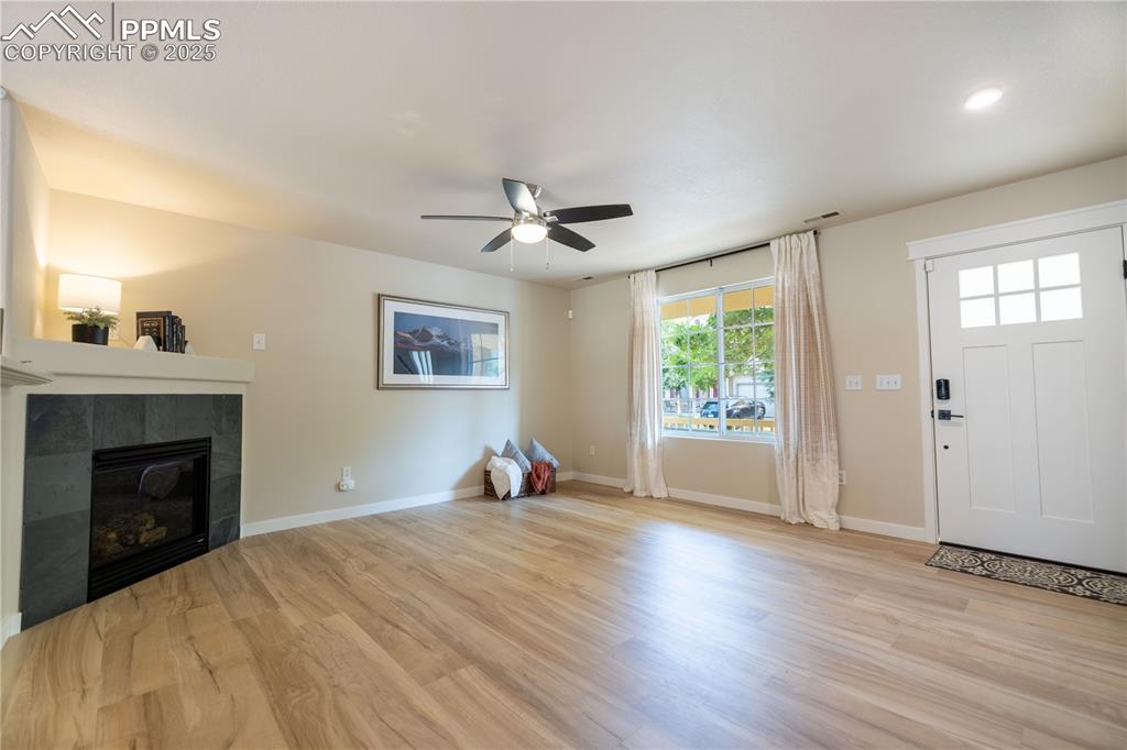 Image 7 of 42: Unfurnished living room with ceiling fan, wood finished floors, a tile fire