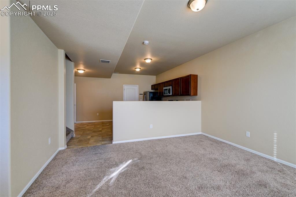 Image 16 of 33: Kitchen with light carpet, open floor plan, dark brown cabinetry, appliance