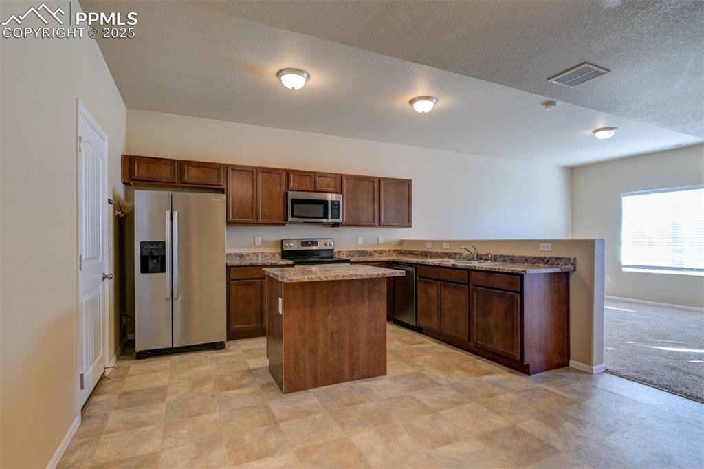 Image 8 of 33: Kitchen with stainless steel appliances, a kitchen island, dark stone count