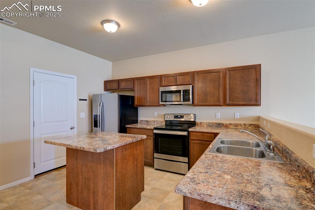 Image 9 of 33: Kitchen with stainless steel appliances, a center island, and brown cabinet