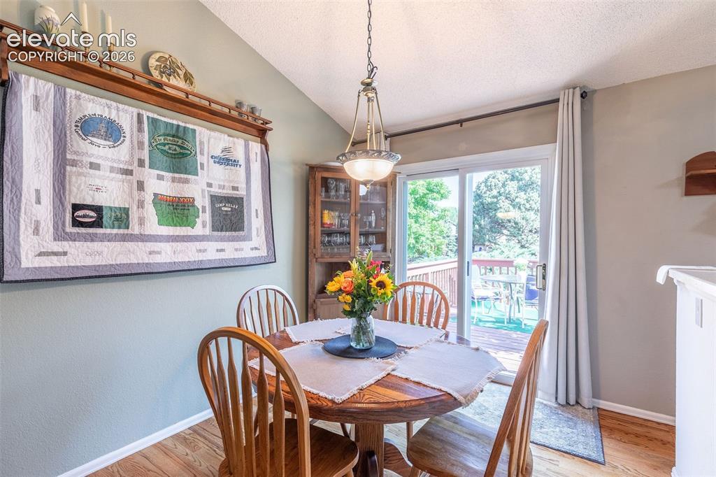 Image 10 of 24: Dining area with wood-finish flooring, vaulted ceiling, and a glass sliding