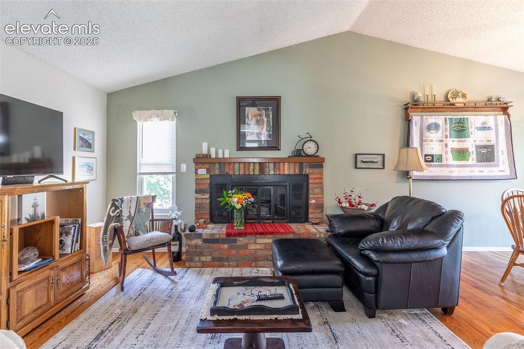 Image 7 of 24: Living area with a vaulted ceiling, brick fireplace, and wood-finish floori
