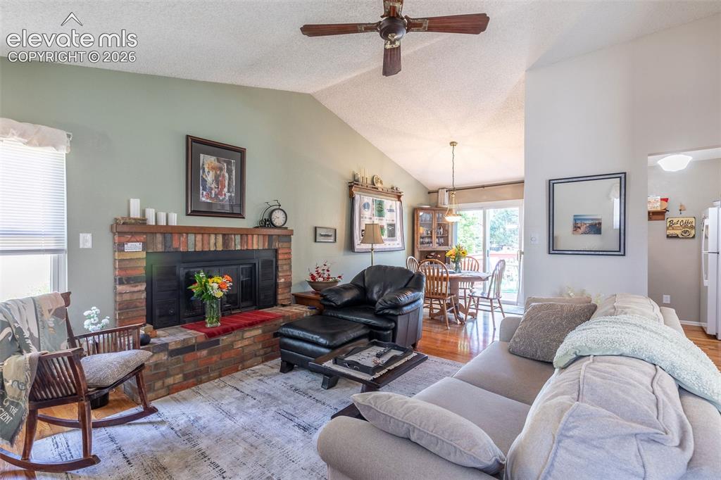 Image 8 of 24: Living space featuring a brick fireplace, vaulted ceiling, and wood-finish