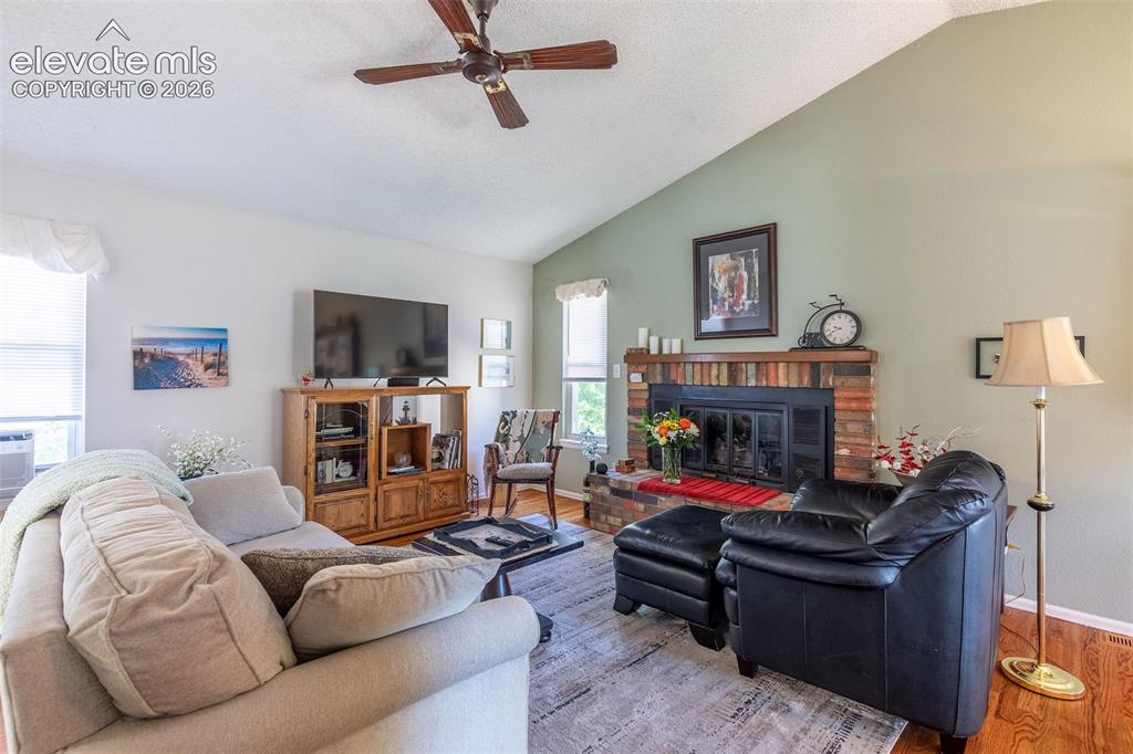 Image 9 of 24: Spacious living area featuring a brick fireplace, vaulted ceiling with a ce
