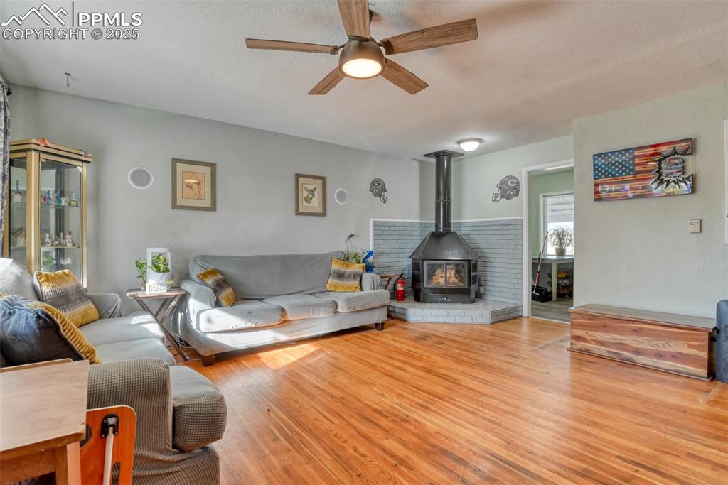 Image 6 of 45: Living area with a wood stove, light wood-style floors, ceiling fan, and a