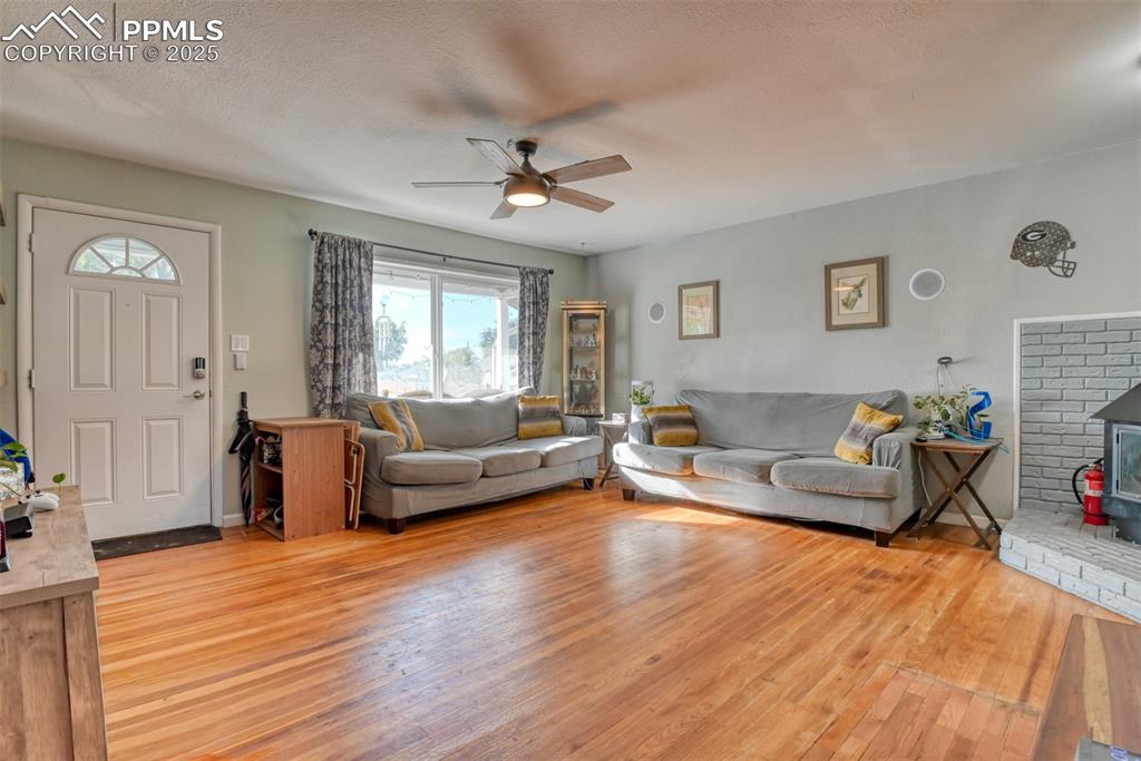 Image 8 of 45: Living room with a wood stove, light wood-style flooring, ceiling fan, and