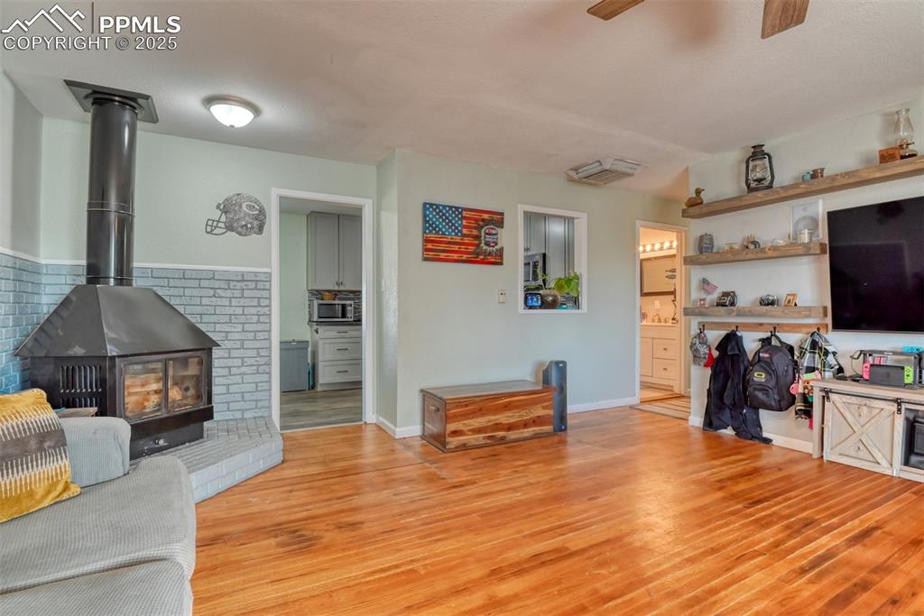 Image 9 of 45: Living area with light wood finished floors, a wood stove, and a ceiling fa
