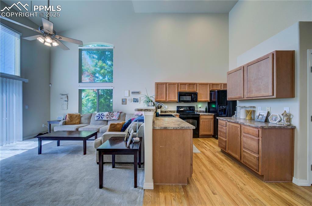 Image 11 of 49: Kitchen with a peninsula, high vaulted ceiling, brown cabinetry, black appl