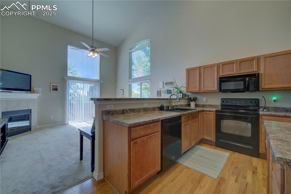 Image 12 of 49: Kitchen featuring black appliances, high vaulted ceiling, a peninsula, a fi