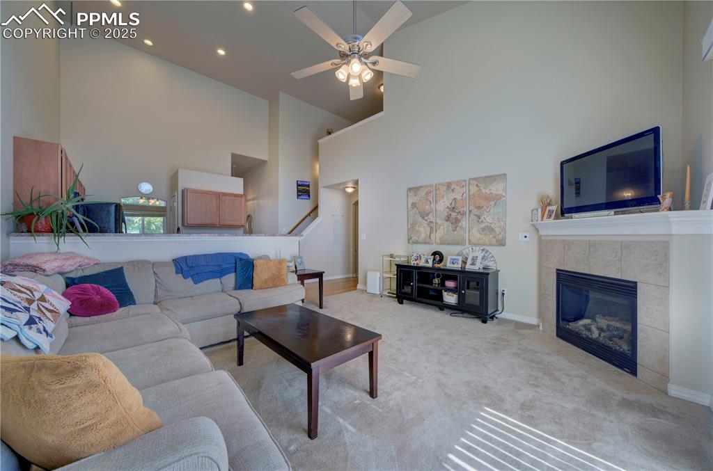 Image 14 of 49: Carpeted living area with a high ceiling, a tile fireplace, a ceiling fan,