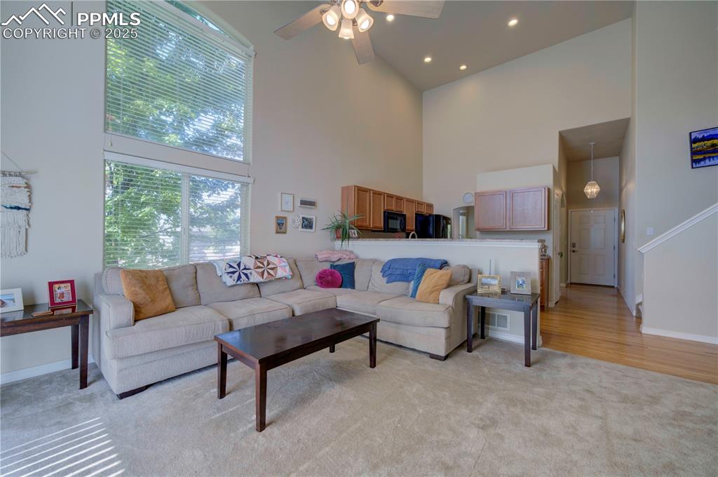 Image 15 of 49: Living area featuring a high ceiling, light carpet, a ceiling fan, and rece