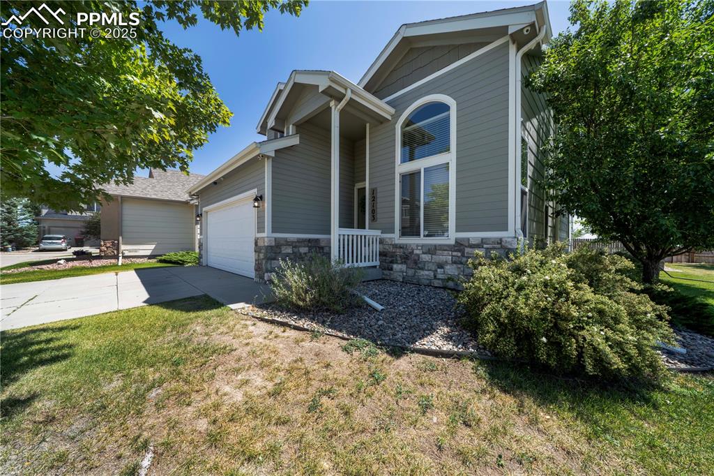 Image 2 of 49: View of front facade with driveway, a garage, stone siding, and a front yar