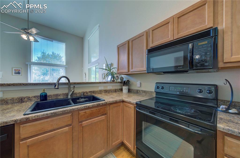Image 8 of 49: Kitchen with black appliances, a ceiling fan, and brown cabinetry
