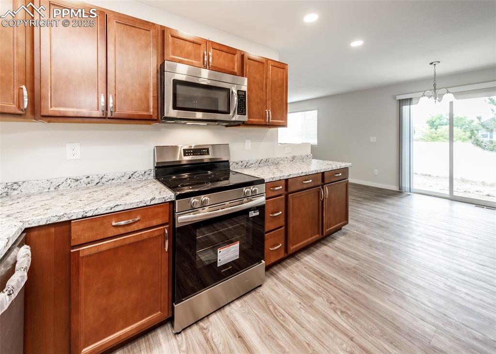 Image 17 of 45: Kitchen featuring stainless steel appliances, brown cabinets, light wood fi