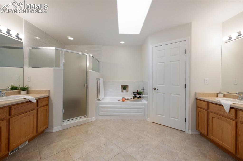 Image 22 of 38: Bathroom featuring a skylight, two vanities, a bath, a stall shower, and li