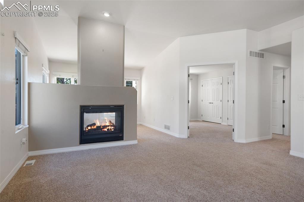 Image 4 of 38: Unfurnished living room featuring light colored carpet, a multi sided firep