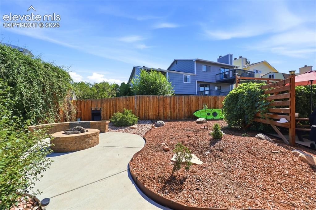 Image 29 of 37: Outdoor patio featuring a built-in stone fire pit, curved concrete pathway,
