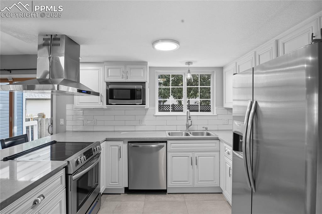 Image 11 of 32: Kitchen with stainless steel appliances, island range hood, white cabinets,