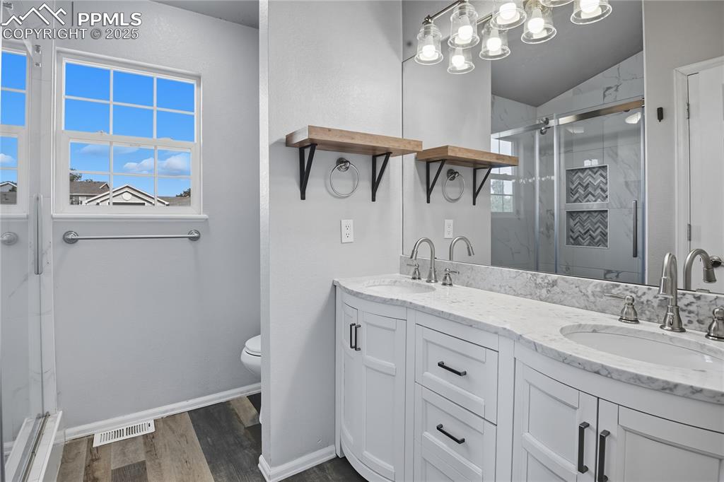 Image 21 of 32: Full bathroom with a stall shower, double vanity, and dark wood finished fl