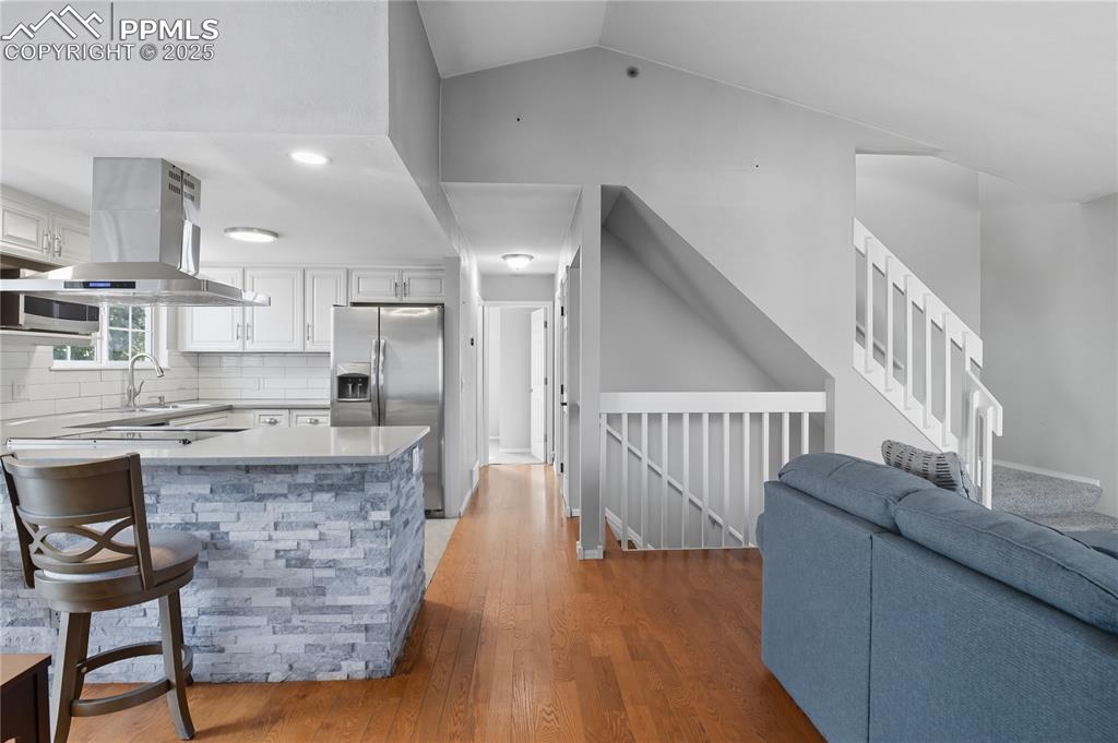 Image 4 of 32: Kitchen featuring light wood finished floors, backsplash, island exhaust ho