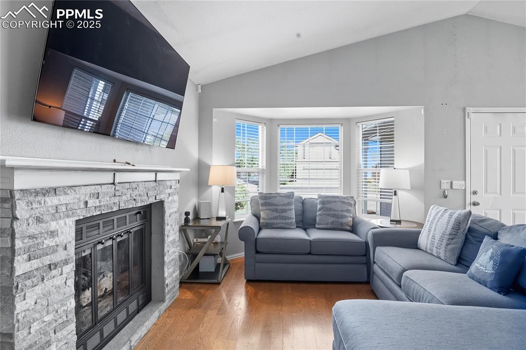 Image 8 of 32: Living area with lofted ceiling, wood finished floors, and a fireplace