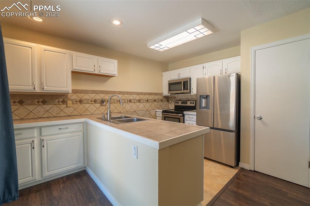 Image 12 of 42: Kitchen with stainless steel appliances, dark wood-type flooring, white cab
