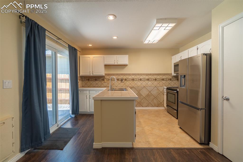 Image 14 of 42: Kitchen with appliances with stainless steel finishes, tile counters, white