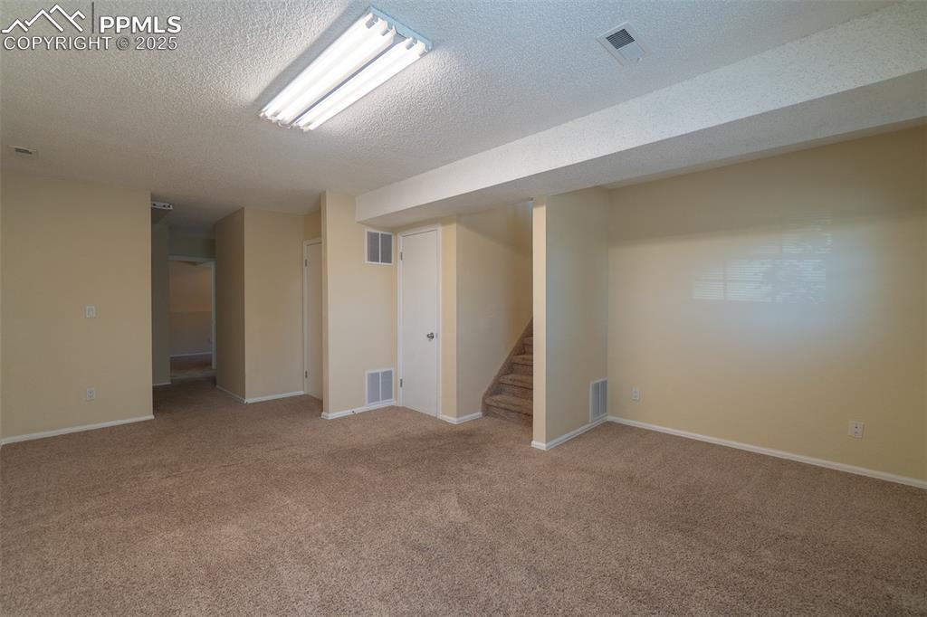 Image 25 of 42: Finished basement featuring carpet floors, stairs, and a textured ceiling