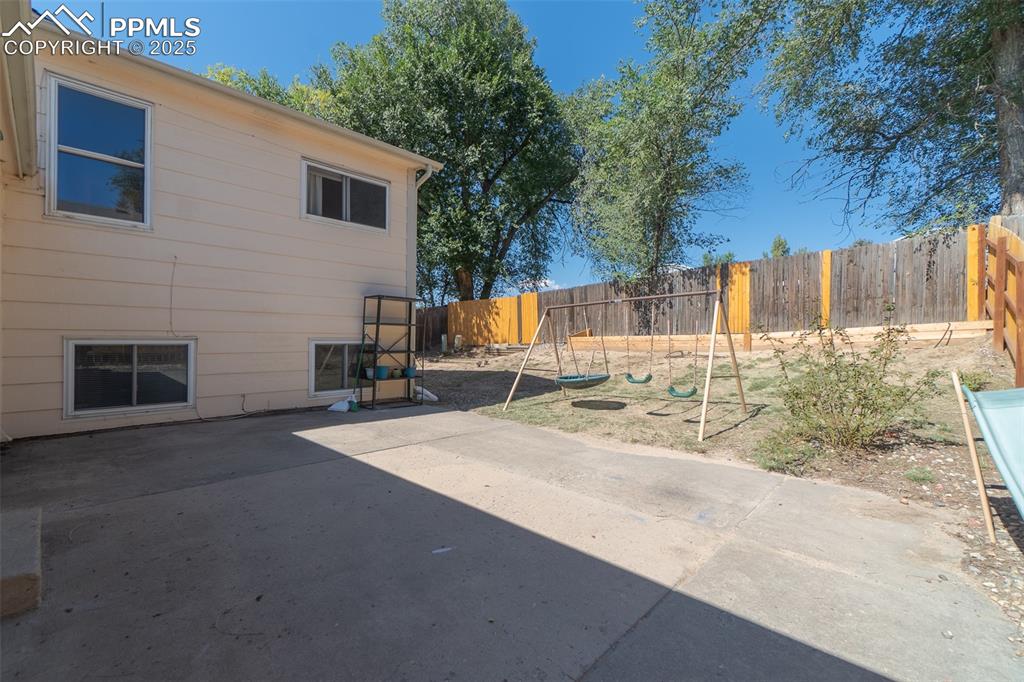 Image 39 of 42: Fenced backyard featuring a playground and a patio area