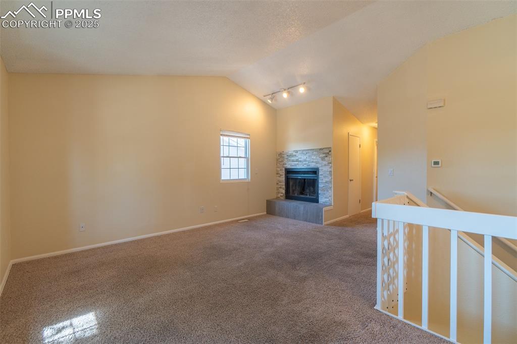 Image 9 of 42: Unfurnished living room featuring vaulted ceiling, carpet, and a tiled fire
