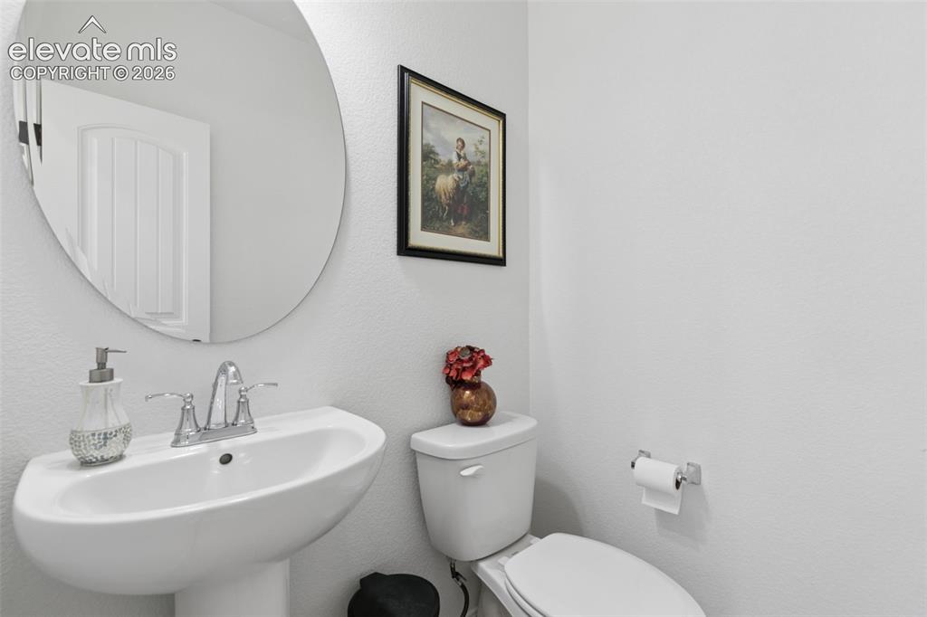 Image 10 of 26: Pedestal sink with chrome faucet, oval wall mirror, and a white toilet