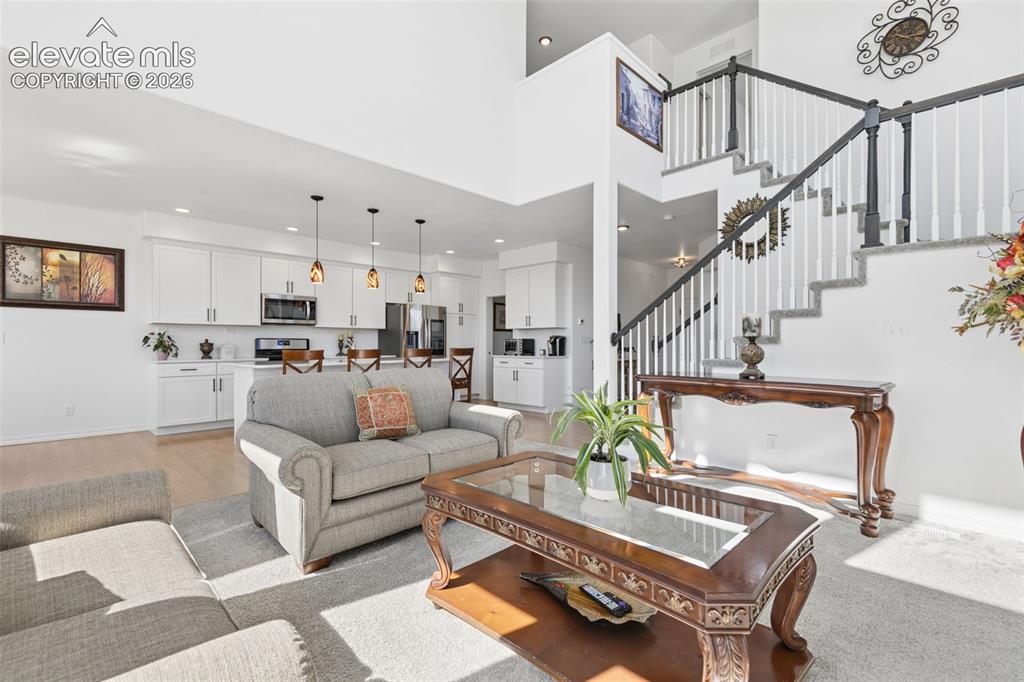 Image 3 of 26: Expansive living area featuring a two-story ceiling, a staircase with dark 