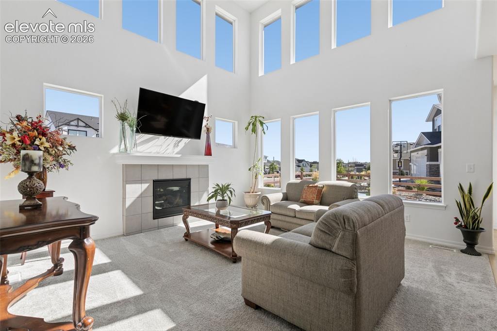 Image 4 of 26: Expansive living space featuring a tiled fireplace, high ceilings, multiple