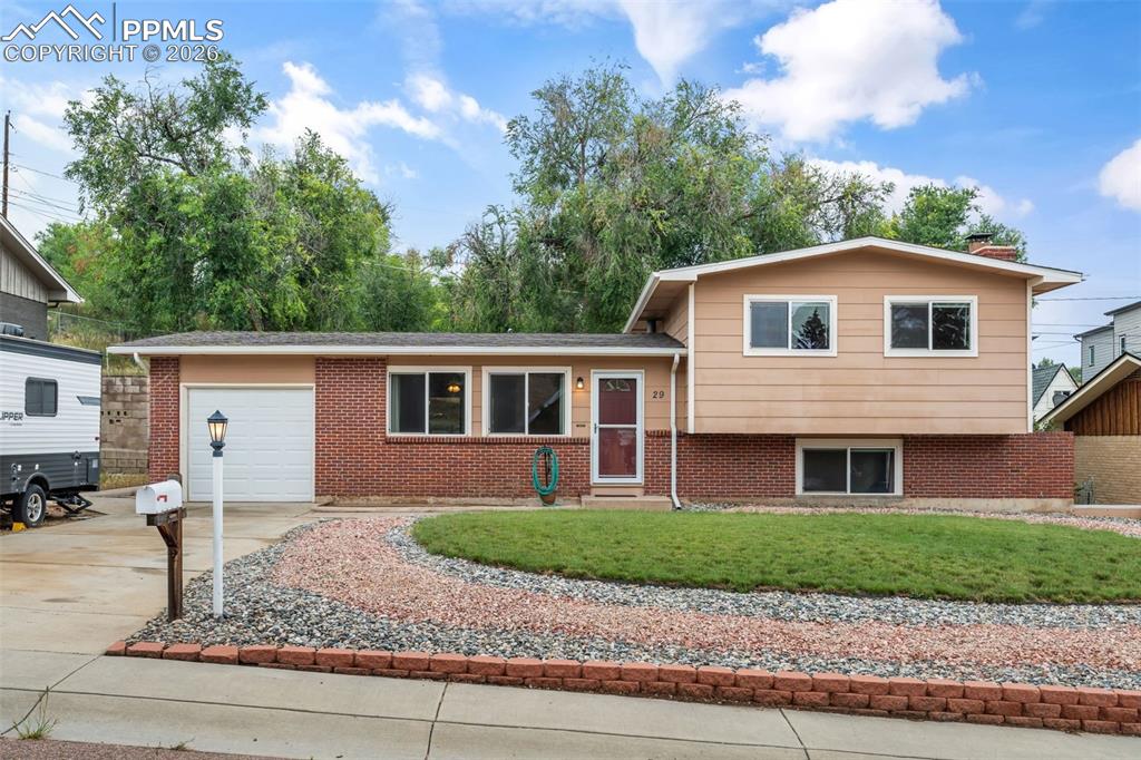 Caption: Split level home with a garage, concrete driveway, a front lawn, and brick siding