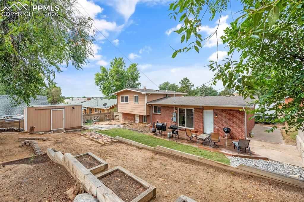 Image 38 of 40: Back of property featuring a shed, a patio, a garden, and brick siding
