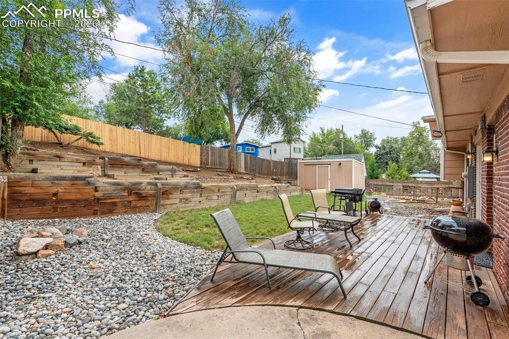 Image 39 of 40: Wooden deck featuring a storage unit, a fenced backyard, and grilling area