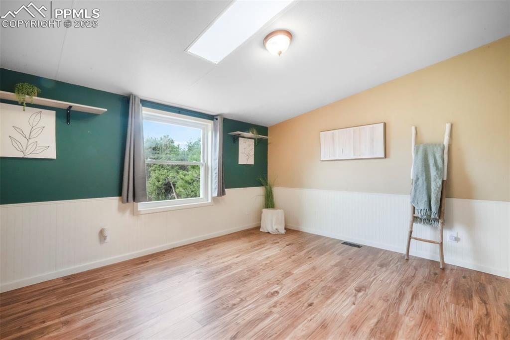Image 27 of 50: Unfurnished room with a wainscoted wall, light wood-style floors, a skyligh