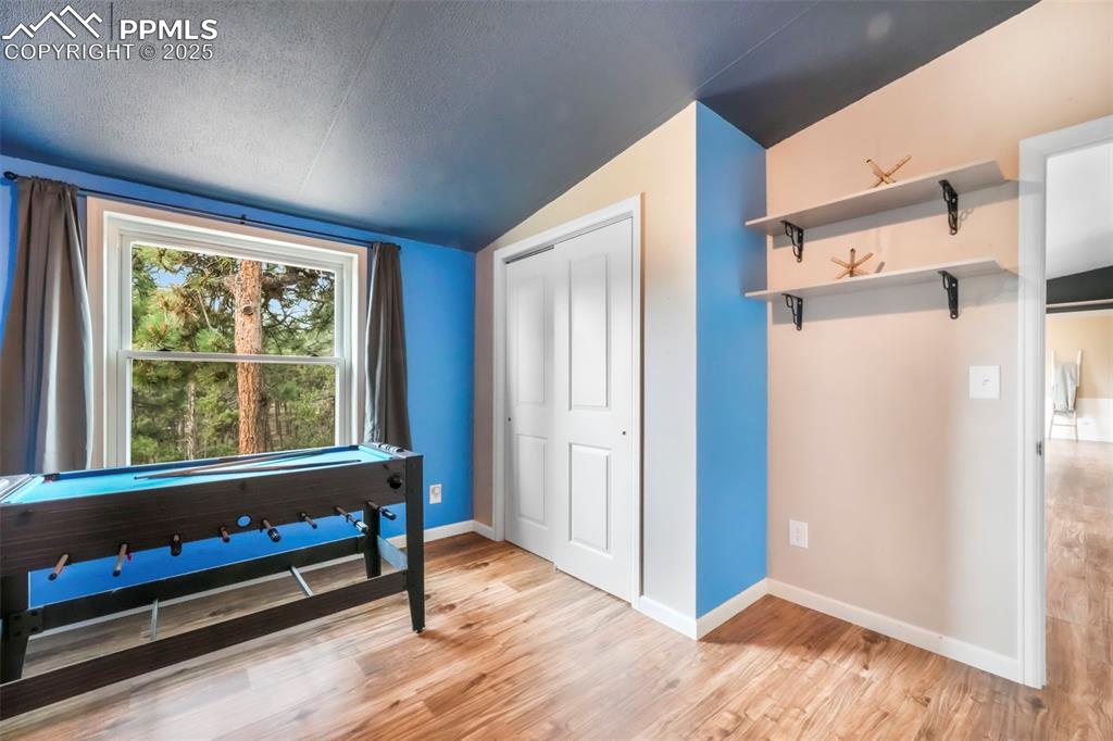 Image 33 of 50: Misc room with a textured ceiling, lofted ceiling, and light wood-type floo