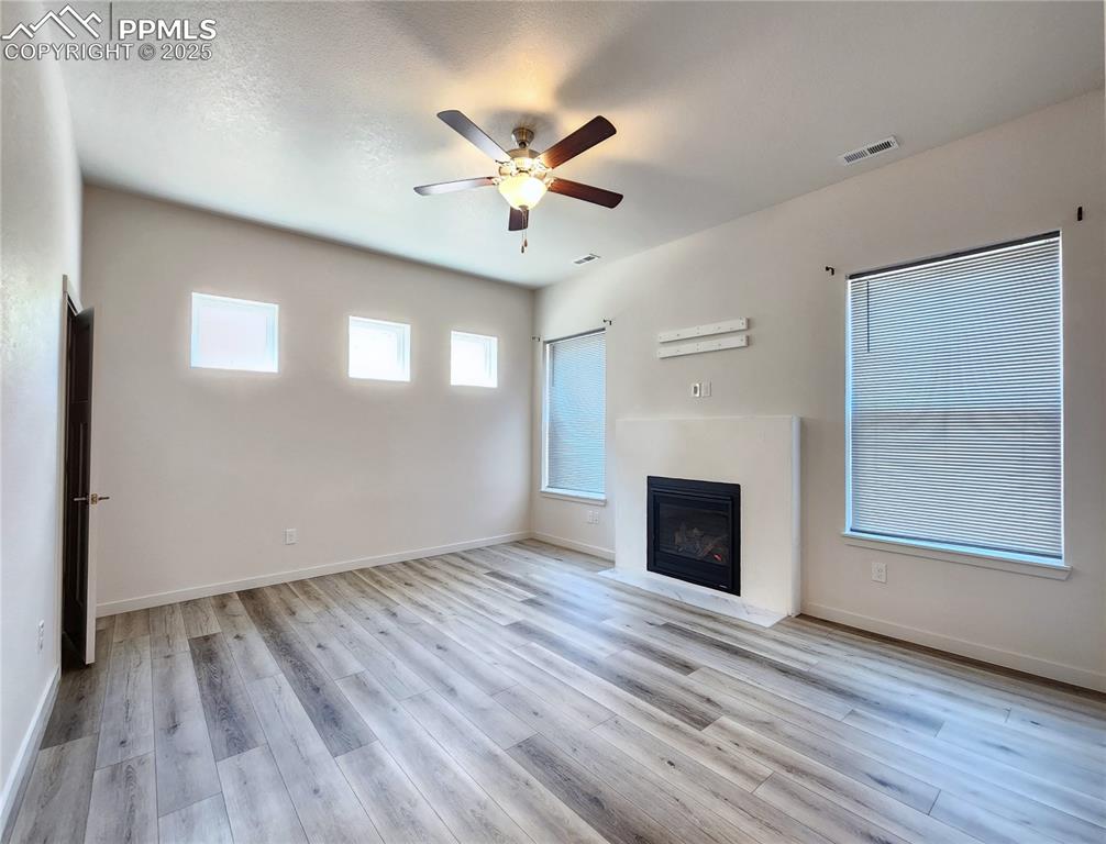 Image 8 of 31: Bright great room with large windows, modern fireplace, and ceiling fan