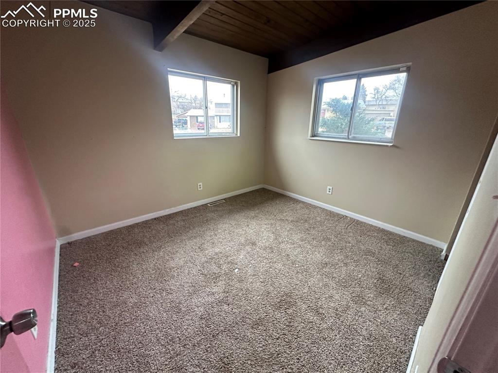 Image 8 of 14: Carpeted spare room with a wood ceiling with exposed beams and baseboards