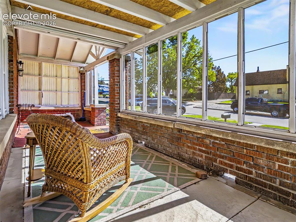 Image 23 of 27: Enclosed front porch featuring brick knee walls, expansive windows, a concr