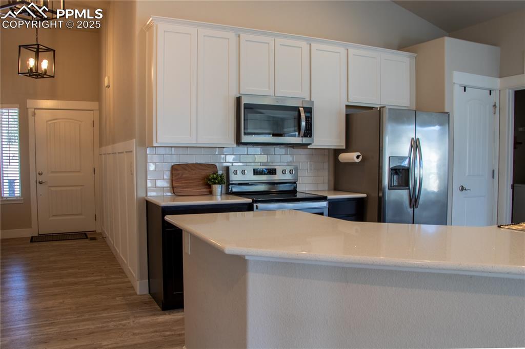 Image 13 of 30: Kitchen with stainless steel appliances, white cabinetry, pendant lighting,