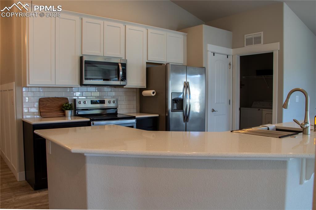 Image 14 of 30: Kitchen with appliances with stainless steel finishes, white cabinets, ligh