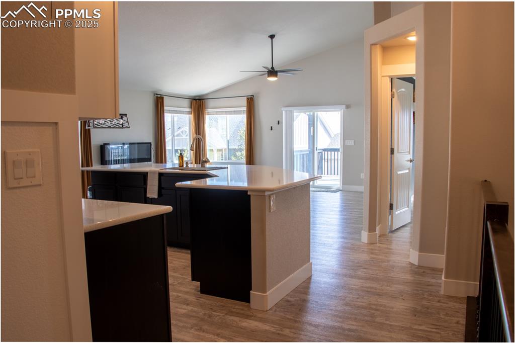 Image 8 of 30: Kitchen featuring dark cabinetry, vaulted ceiling, light wood-style floors,