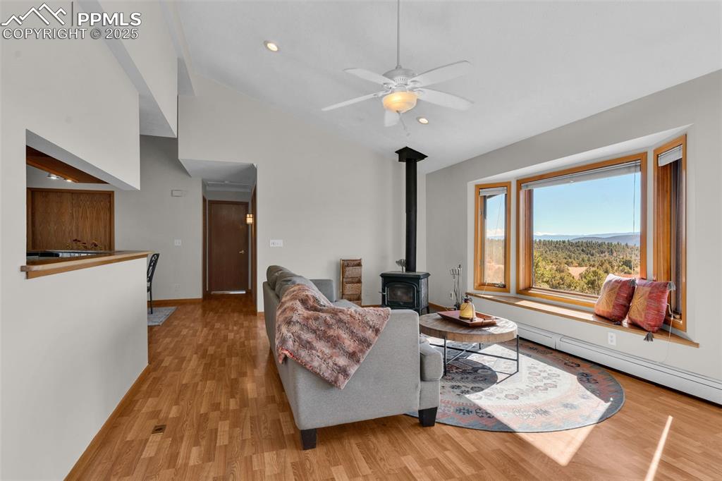 Image 10 of 50: Living area featuring light wood-style flooring, a wood stove, high vaulted