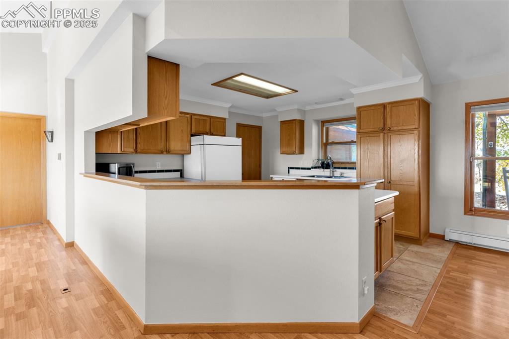 Image 12 of 50: Kitchen featuring brown cabinetry, freestanding refrigerator, light wood-ty