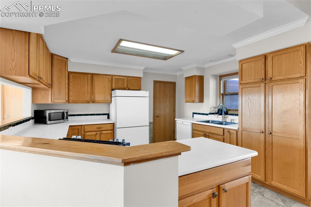 Image 13 of 50: Kitchen with light countertops, ornamental molding, white appliances, a pen