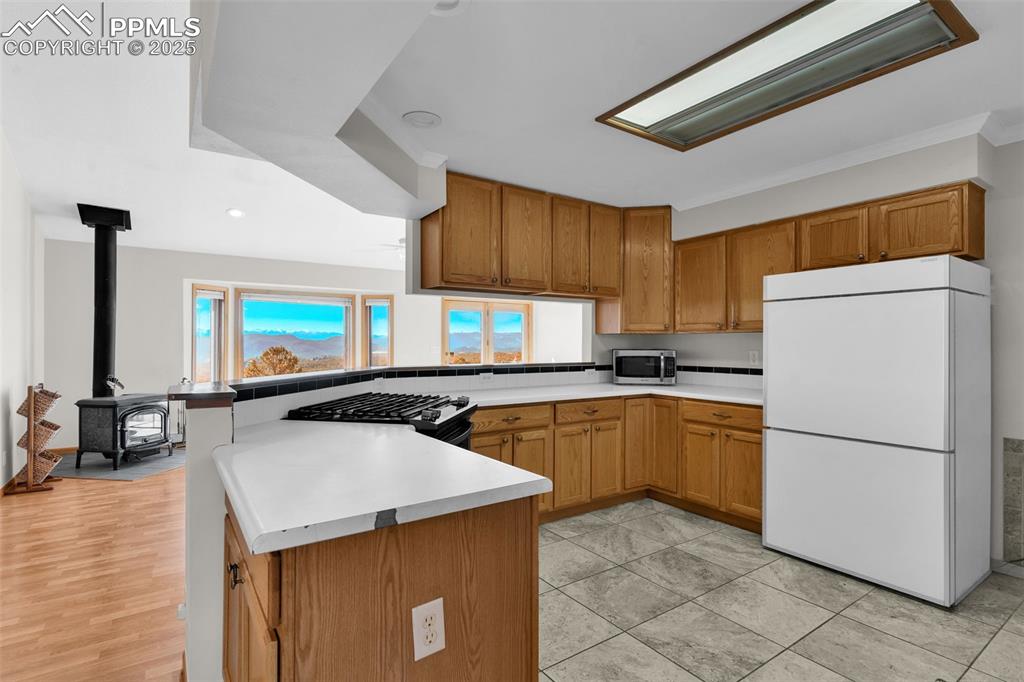 Image 15 of 50: Kitchen featuring freestanding refrigerator, brown cabinetry, a wood stove,