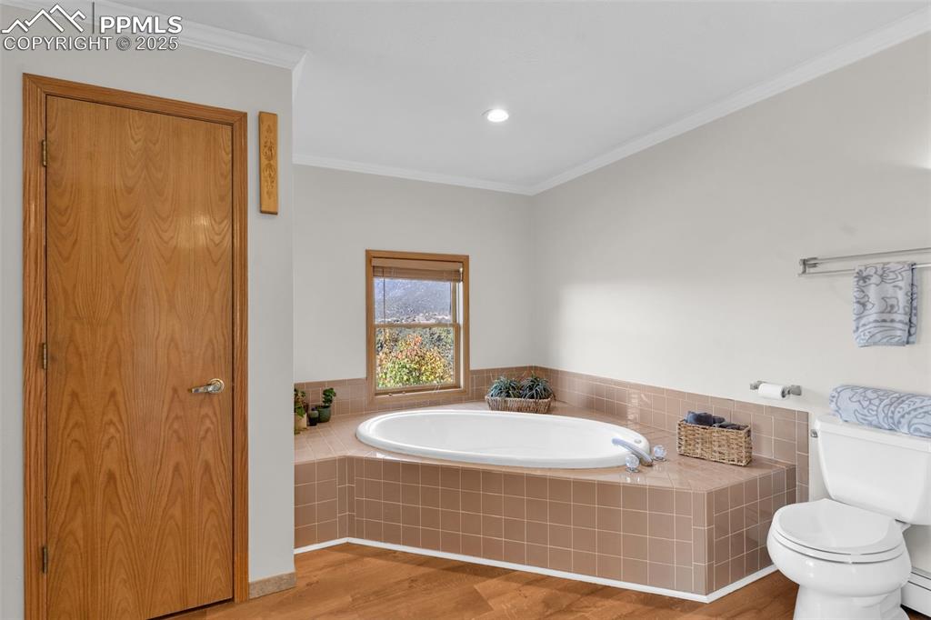 Image 22 of 50: Bathroom with light wood finished floors, ornamental molding, a garden tub,