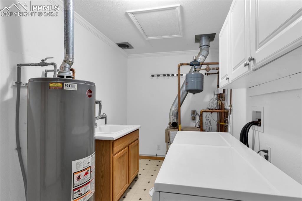 Image 30 of 50: Laundry room featuring cabinet space, gas water heater, ornamental molding,